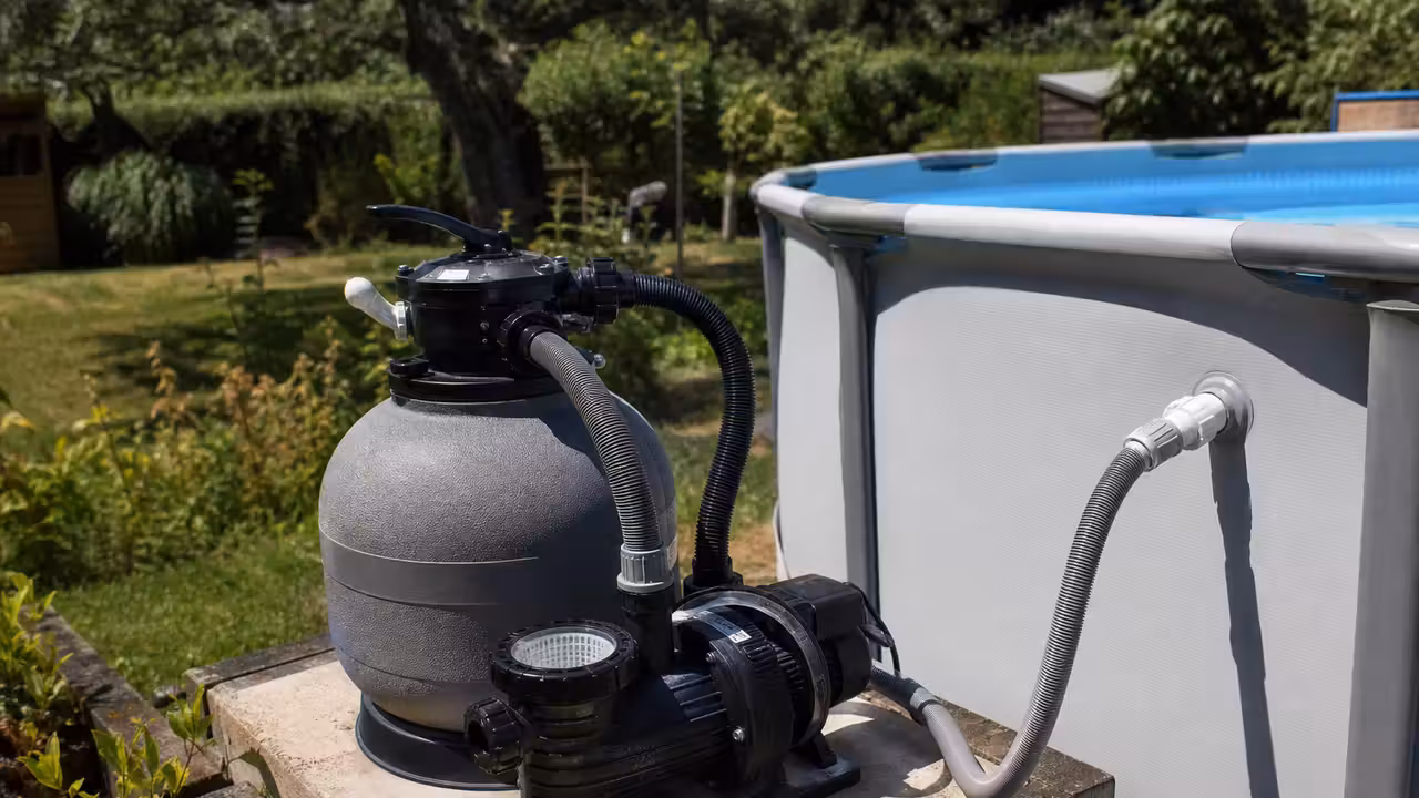 Groupe de filtration à sable compact installé à côté d’une petite piscine hors-sol dans un jardin.