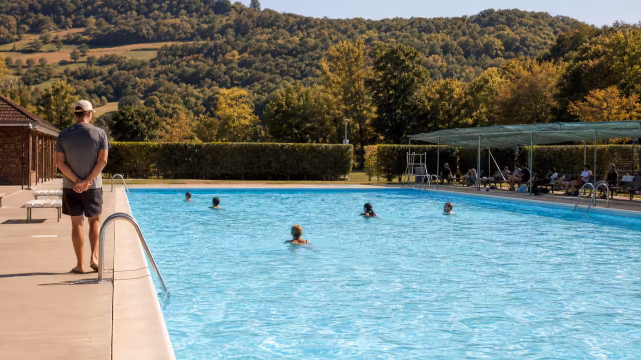 Bassin extérieur de piscine publique avec nageurs de dos et maître-nageur surveillant depuis la plage
