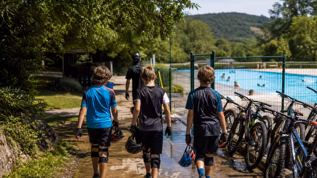Jeunes cyclistes équipés rejoignant une piscine extérieure après une sortie VTT estivale encadrée