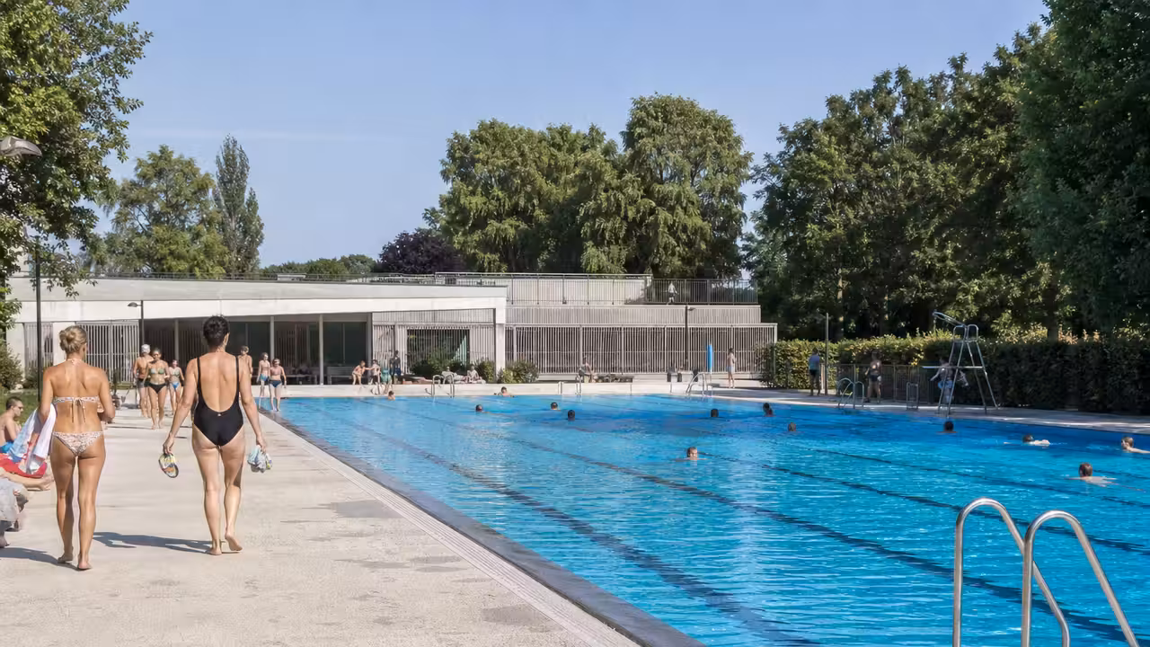 Bassin extérieur fréquenté lors d’une journée estivale dans une piscine municipale, avec lignes de nage et plage