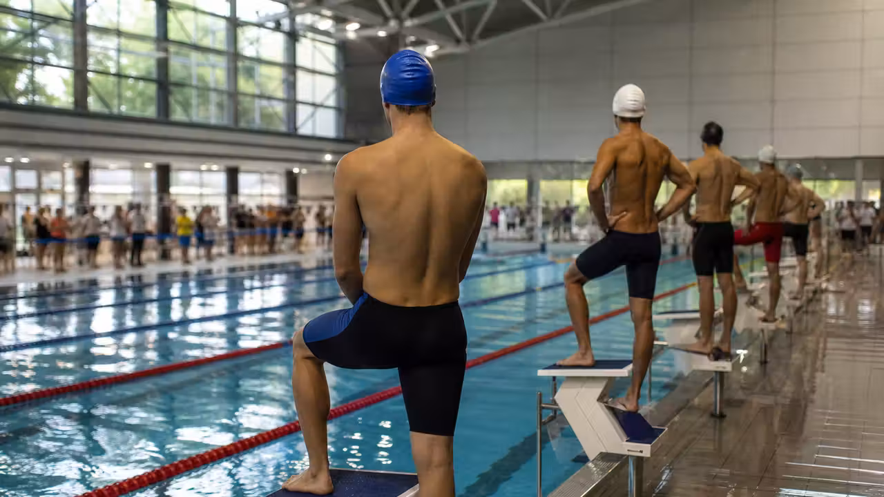 Nageurs équipés de bonnets et de lunettes se préparant au départ d'une compétition dans un bassin couvert