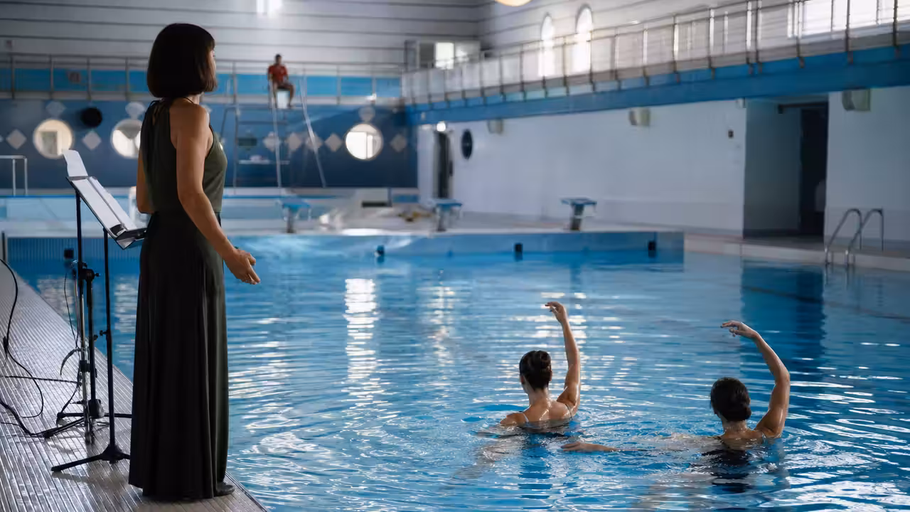 Interprètes évoluant dans un bassin couvert pendant une répétition de spectacle aquatique éclairée en bleu
