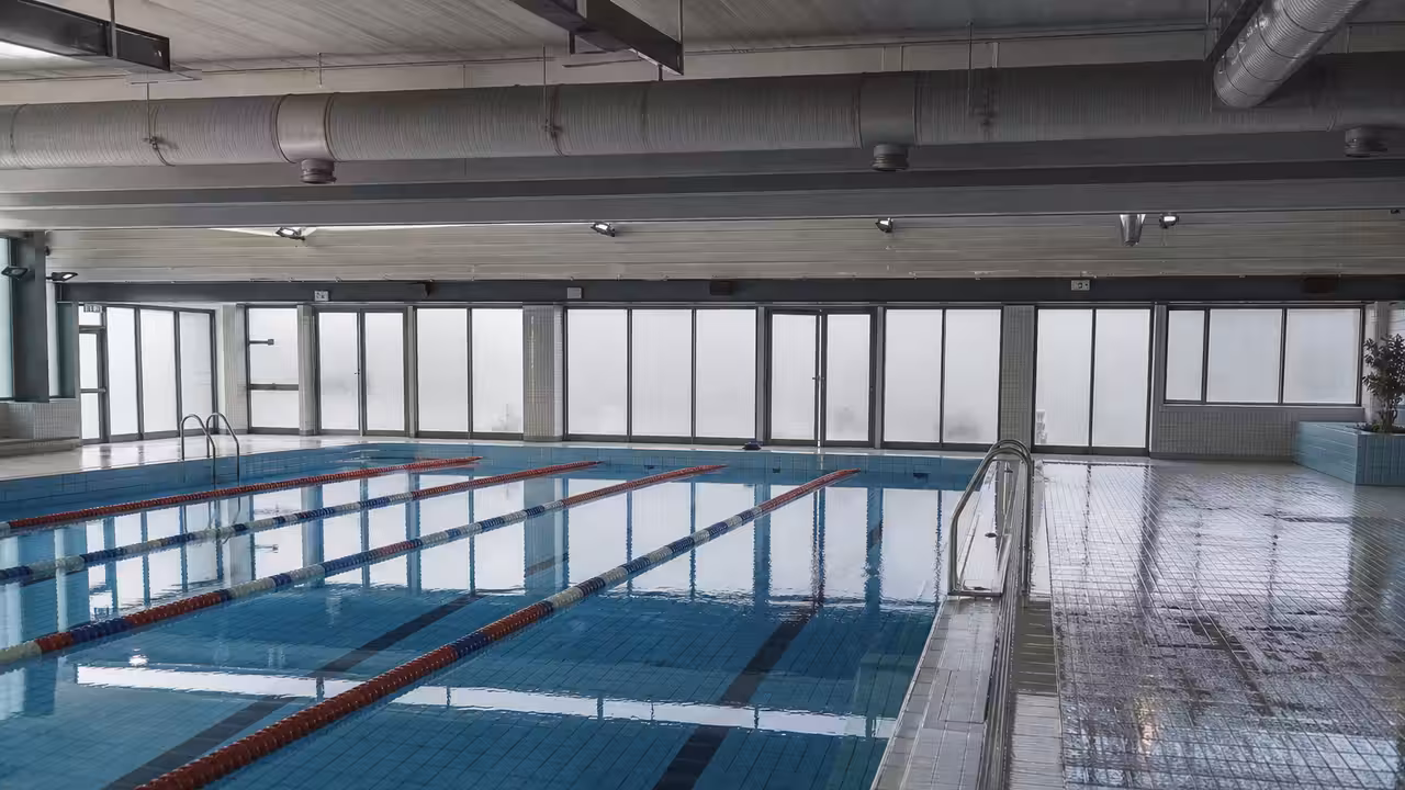 Bassin couvert municipal vide, lignes d’eau calmes et système de ventilation visible au plafond