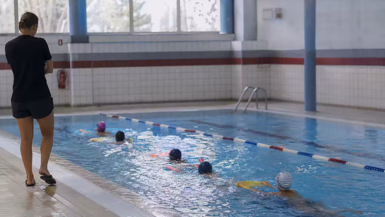 Élèves en séance de natation encadrée dans un bassin intérieur, avec lignes d’eau et maître-nageur au bord
