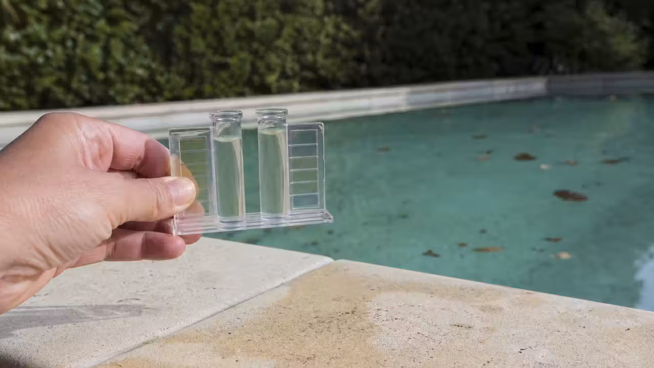 Main tenant un comparateur d'analyse aux tubes d'eau incolore au bord d'une piscine parsemée de feuilles