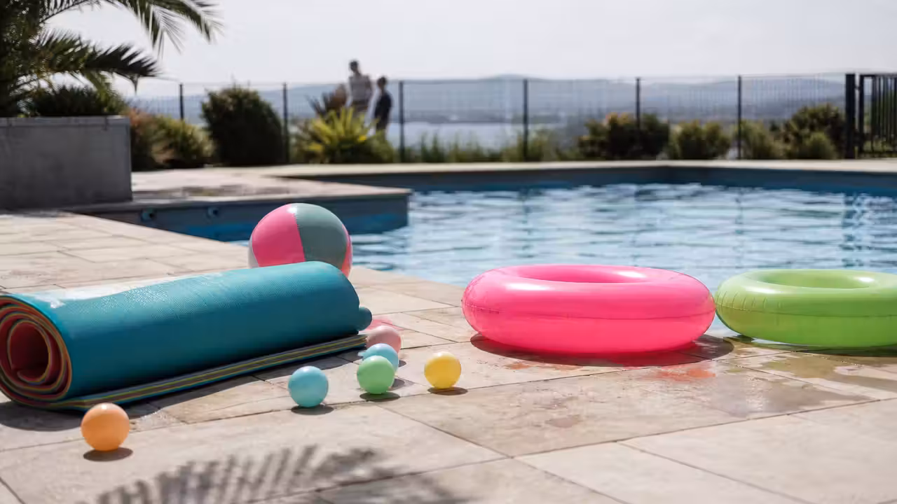 Ballons, anneaux flottants et tapis de jeu rangés au bord d’une piscine familiale sécurisée