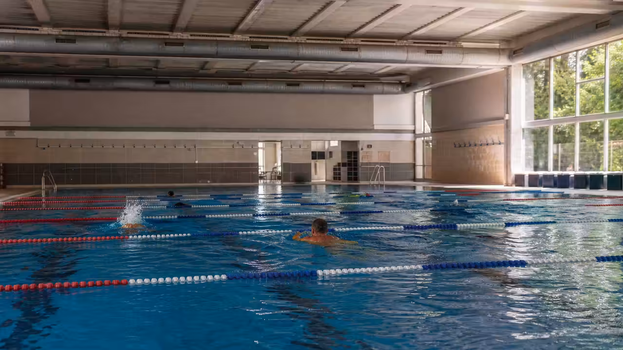 Piscine municipale des années 1970 rénovée, avec bassin couvert et lumière naturelle sur les lignes d’eau