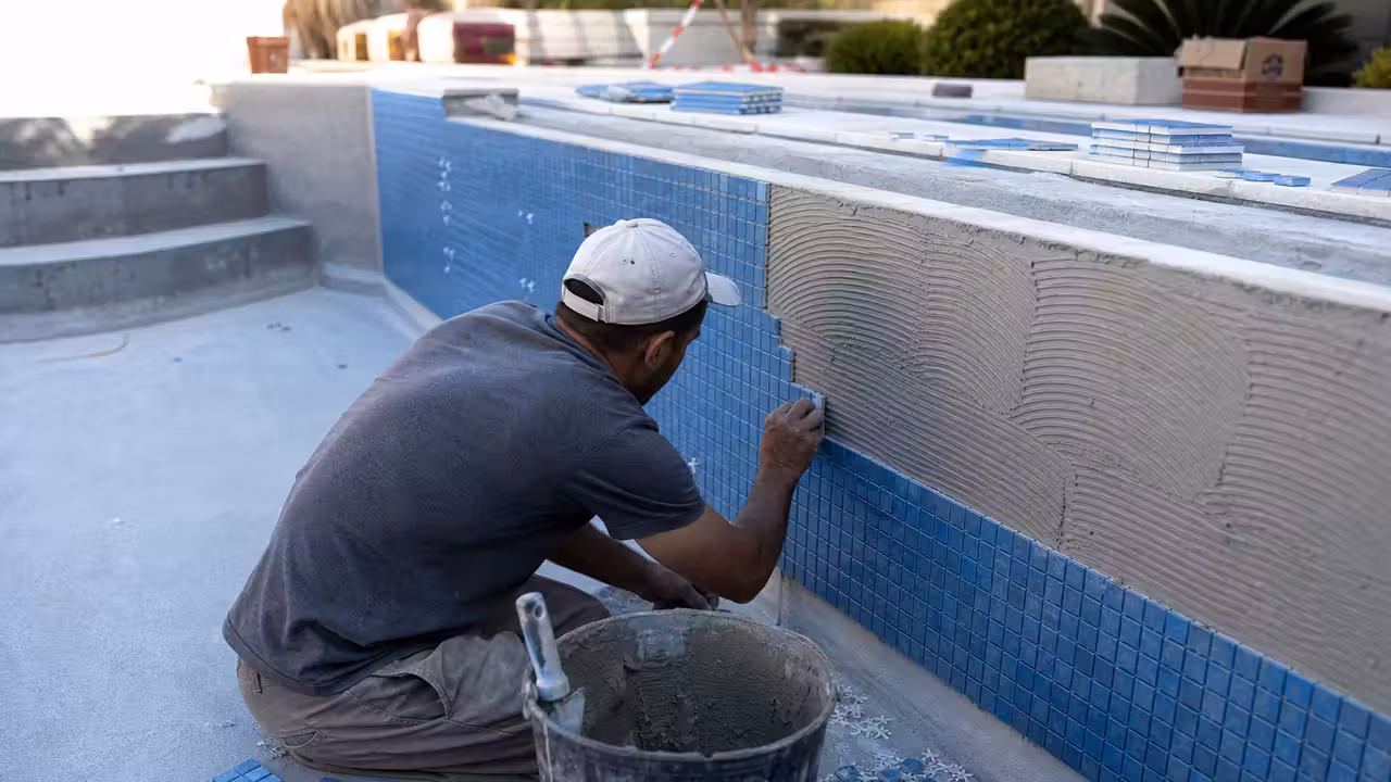 Carreleur posant de petits carreaux bleus sur la paroi préparée d’une piscine en béton vide