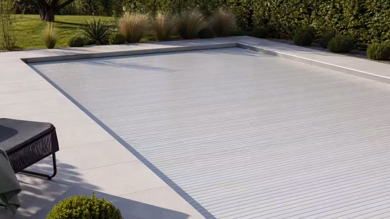Piscine extérieure couverte par un volet roulant, entourée d’une terrasse et d’une végétation sobre