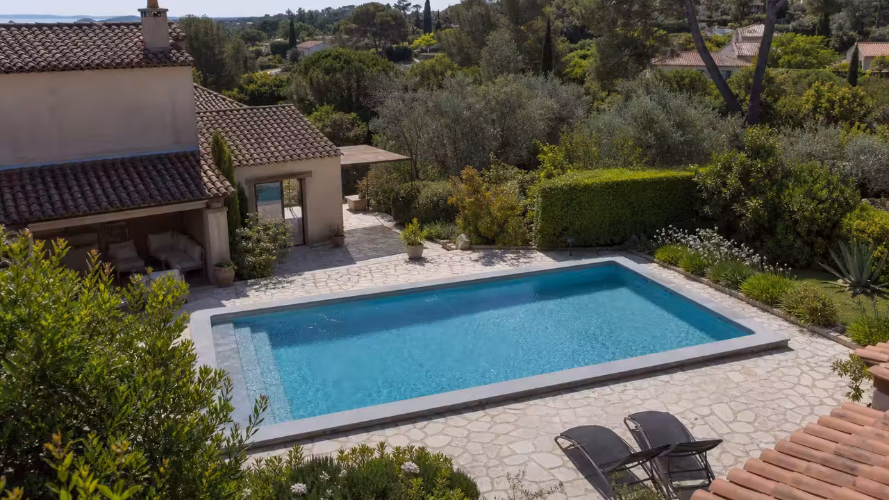 Vue aérienne d’une maison avec piscine enterrée bleue au milieu d’un jardin résidentiel français
