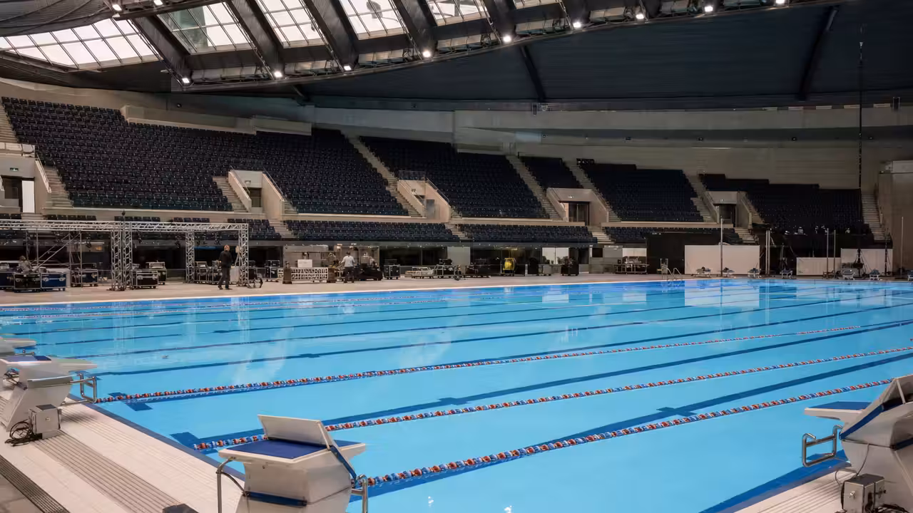 Bassin de compétition temporaire installé dans une grande arena, avec lignes d’eau et gradins à l’arrière-plan