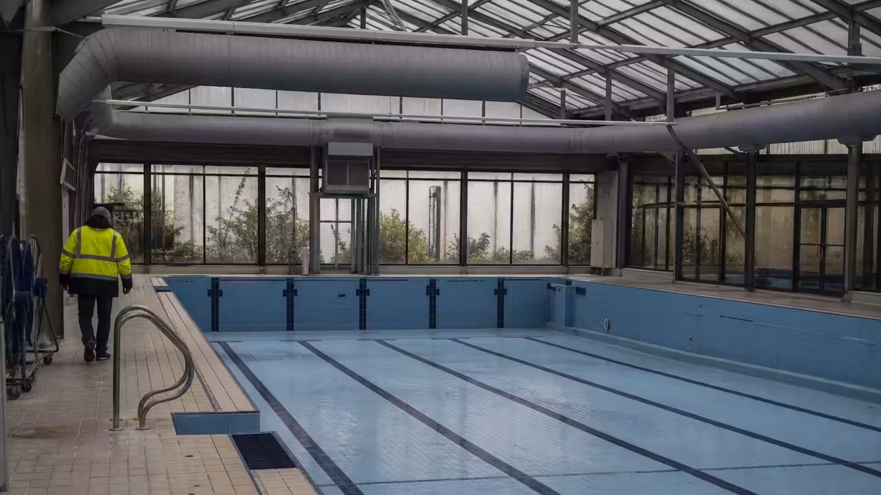 Bassin intérieur ancien d’une piscine municipale, avec verrière, lignes d’eau et plages carrelées vides