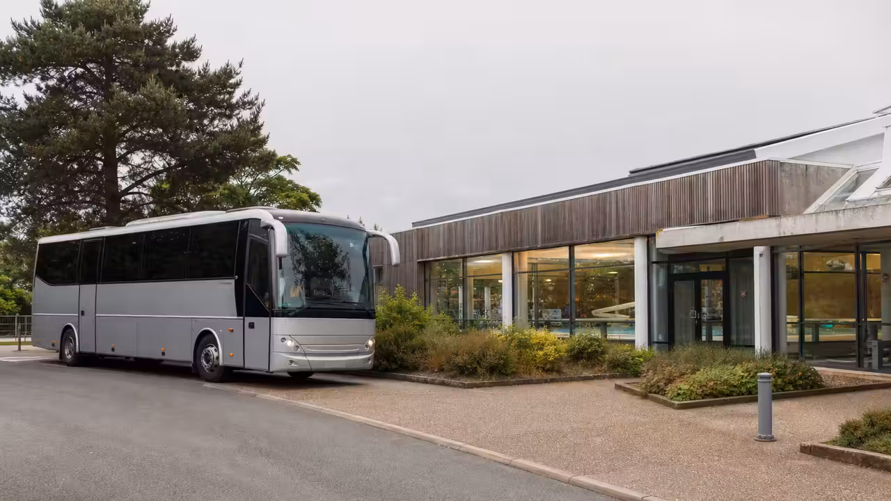 Autocar scolaire devant un centre aquatique public, avec bassin couvert visible en arrière-plan