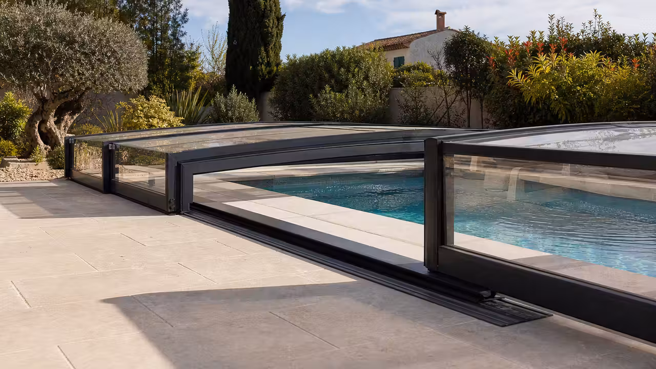 Abri télescopique bas en aluminium et polycarbonate couvrant une piscine dans un jardin paysager