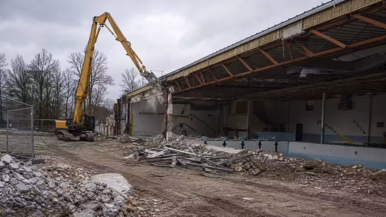 Engin de chantier retirant la toiture d’une ancienne piscine municipale en cours de déconstruction