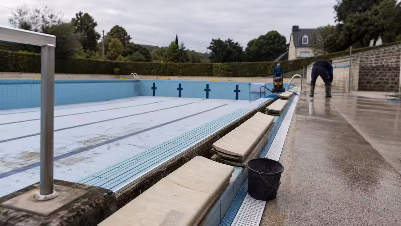 Bassin extérieur municipal vidé pendant sa remise en état, avec goulottes et plages nettoyées avant réouverture