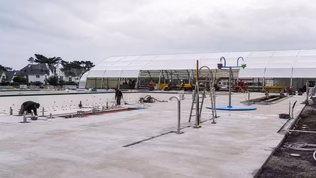 Bassin de piscine municipale en rénovation, protégé par une tente blanche avec plages en béton neuf