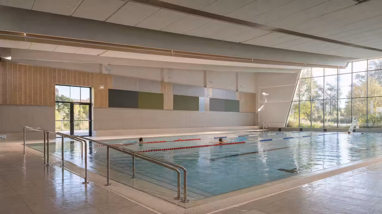 Halle de bassin municipale rénovée avec lignes de nage, accès progressif et lumière naturelle