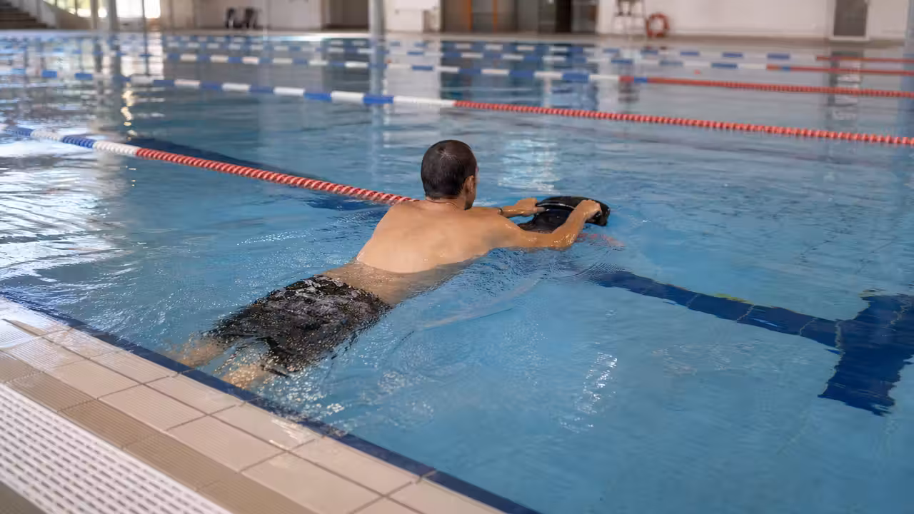 Un adulte utilise un propulseur aquatique dans un couloir réservé d’une piscine municipale surveillée.
