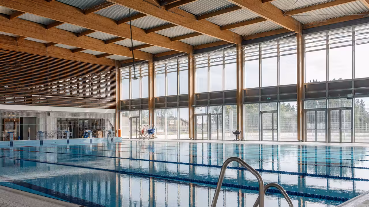 Vue intérieure d’un bassin sportif public de 50 mètres, avec lignes d’eau et grandes baies vitrées.