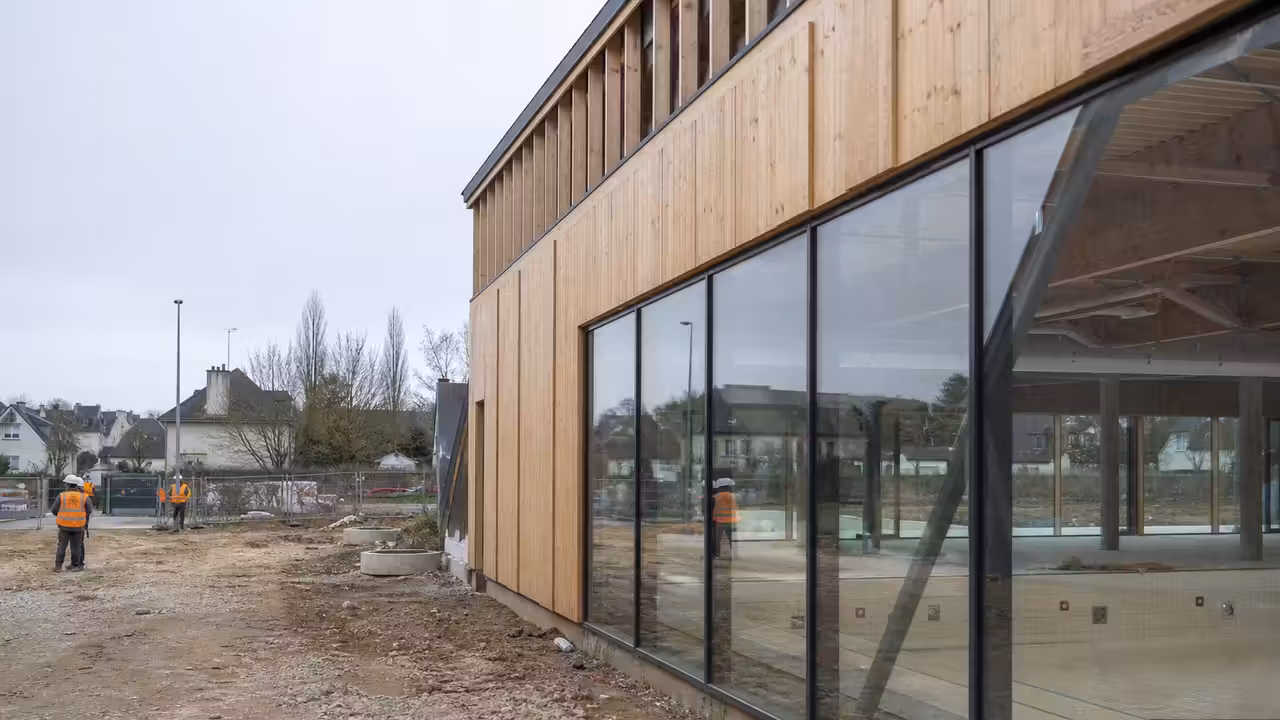 Chantier d’un centre aquatique public contemporain avec structure vitrée et bassin visible à l’arrière-plan
