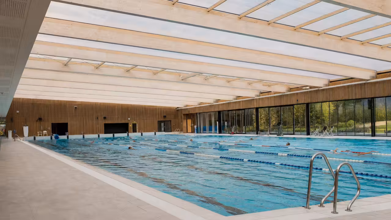 Intérieur lumineux d’une piscine publique rénovée avec grand bassin, lignes d’eau et plafond translucide