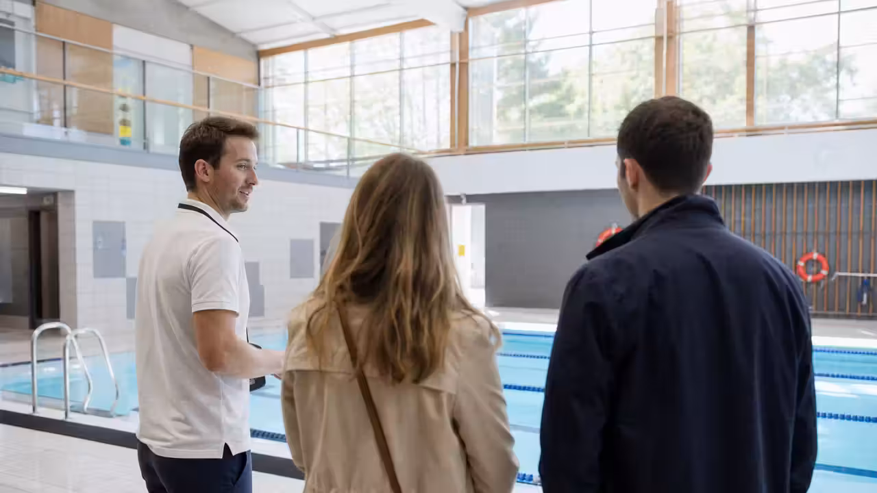 Maître-nageur échangeant avec des visiteurs au bord d’un bassin de piscine municipale