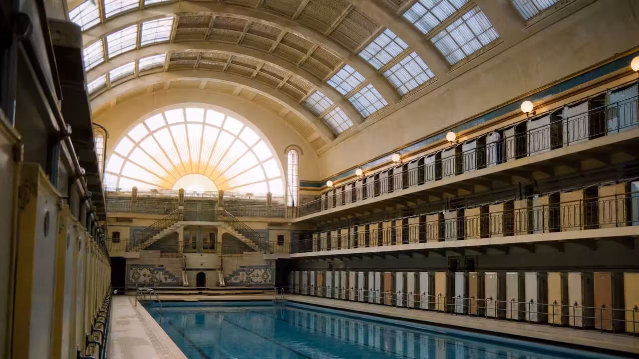 Bassin couvert historique aux faïences claires et cabines superposées dans une piscine parisienne des années 1930
