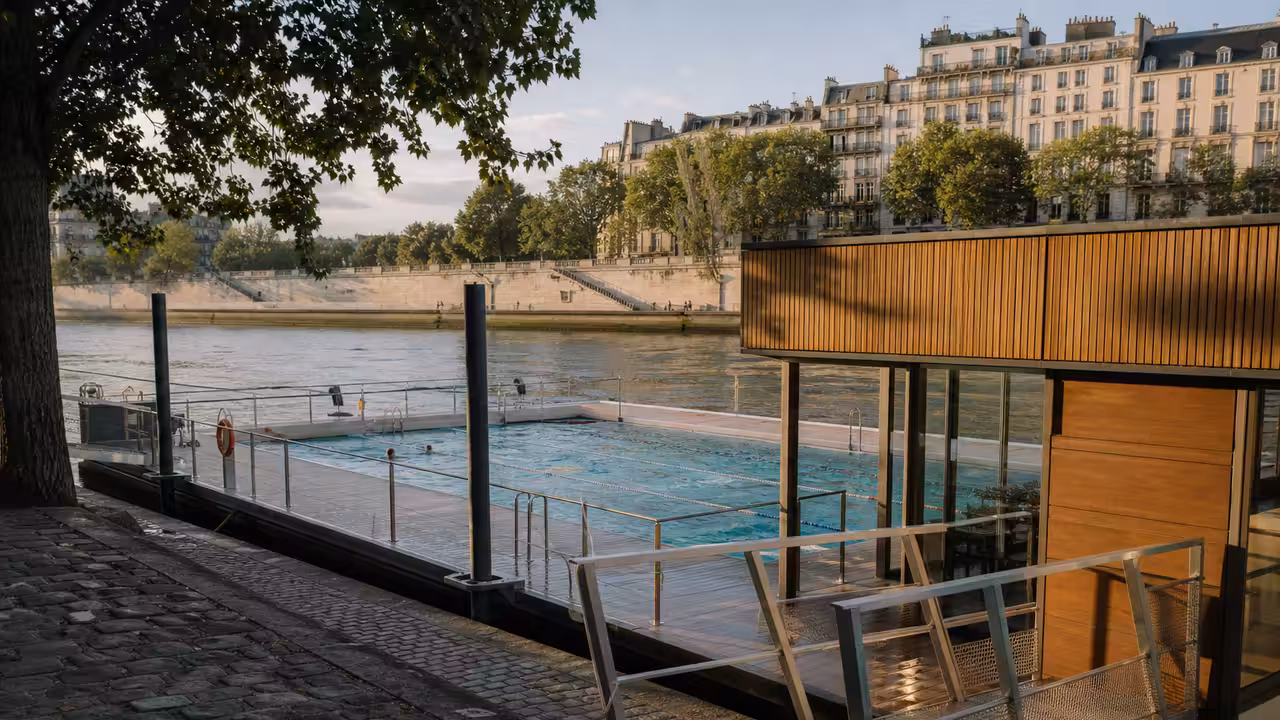 Piscine flottante contemporaine amarrée sur la Seine avec bassin extérieur et quais parisiens en arrière-plan
