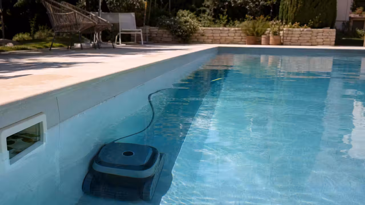 Robot électrique nettoyant le fond et une paroi d’une piscine familiale aux margelles en pierre claire
