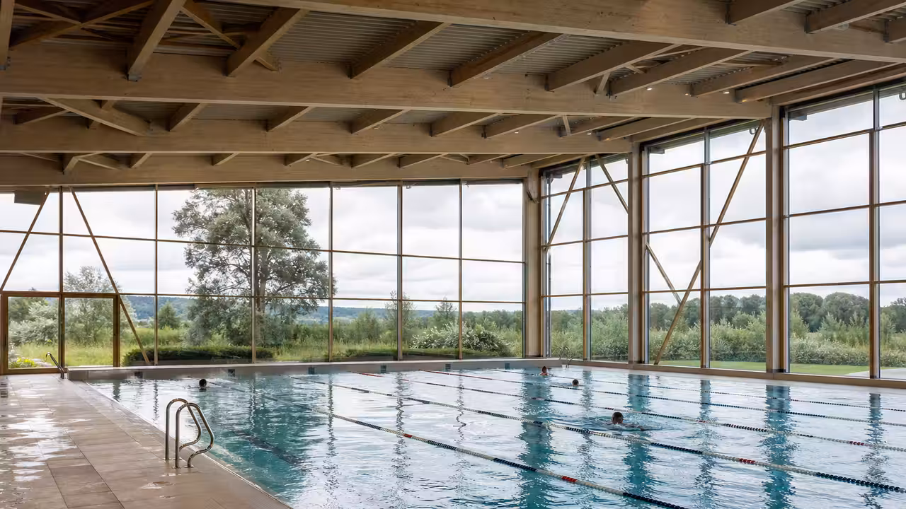 Halle vitrée d’un centre aquatique moderne avec bassin intérieur et lumière naturelle sur le paysage