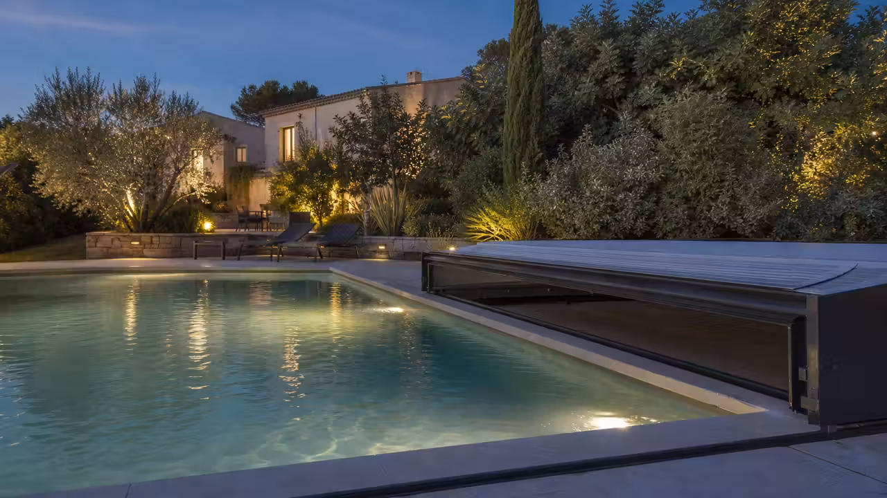Piscine contemporaine au crépuscule, abri discret ouvert et éclairage doux sur les margelles minérales