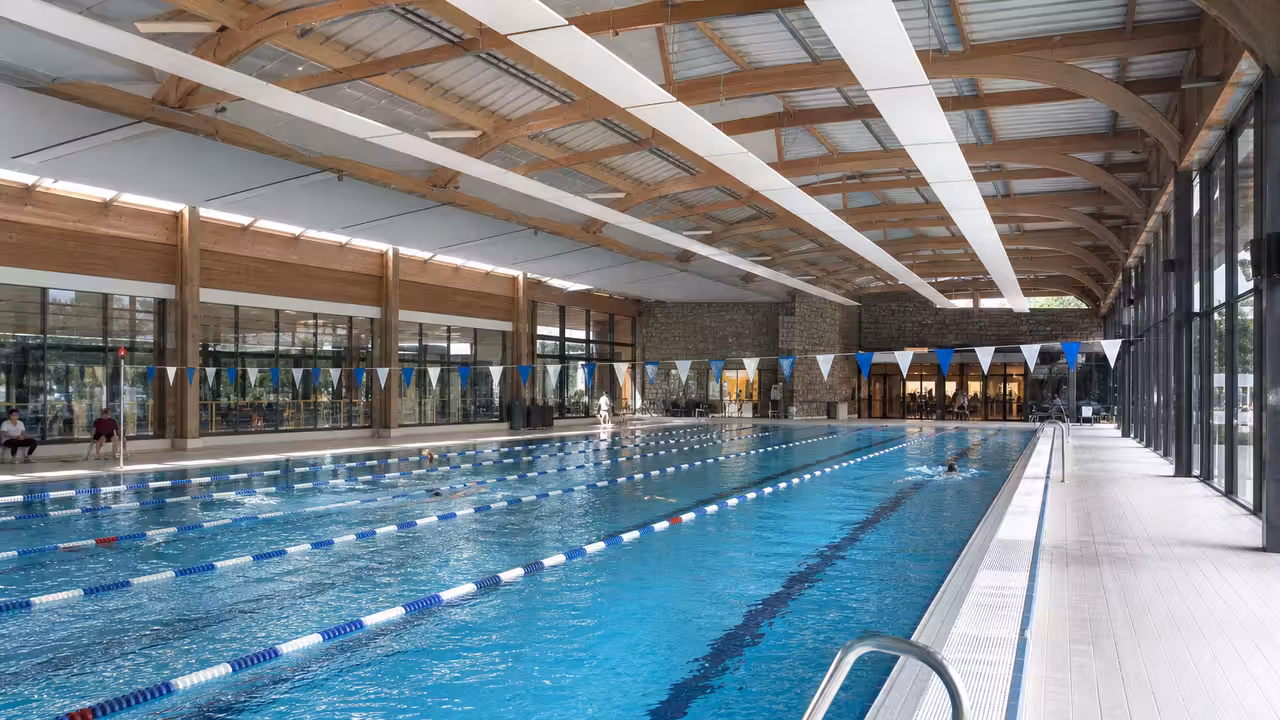 Bassins d’une piscine publique avec lignes d’eau, vestiaires lumineux et baigneurs flous au loin