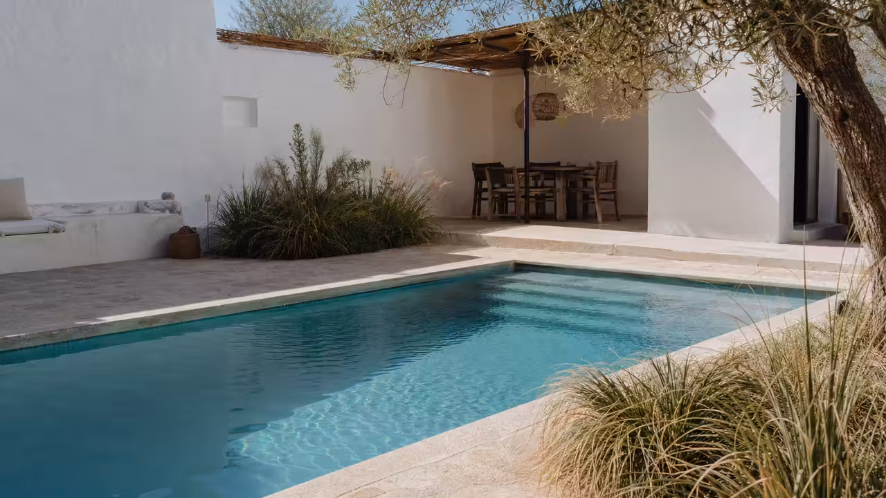 Piscine rectangulaire compacte bordée de pierre claire dans le jardin d’une maison blanche méditerranéenne