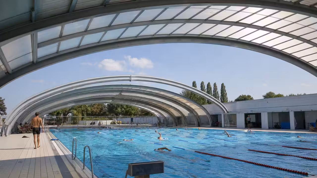 Coupole ouverte d’une piscine municipale avec bassin de nage et baigneurs en été aux Lilas
