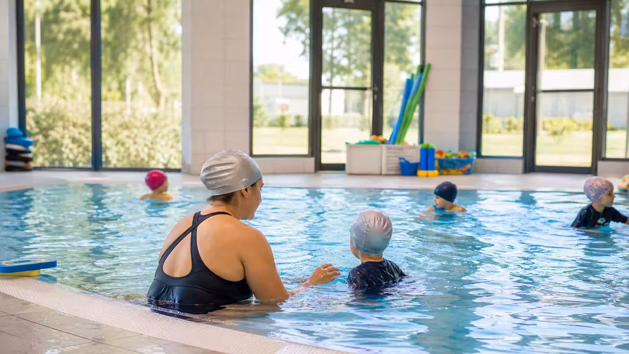Jeune enfant accompagné par un maître-nageur lors d’un exercice ludique d’aisance dans un bassin peu profond