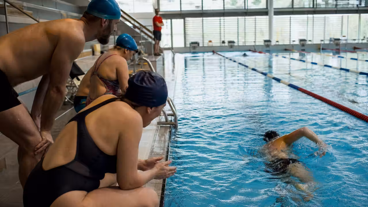 Équipe de nageurs adultes se relayant dans les lignes d’eau d’une piscine lors d’un défi solidaire
