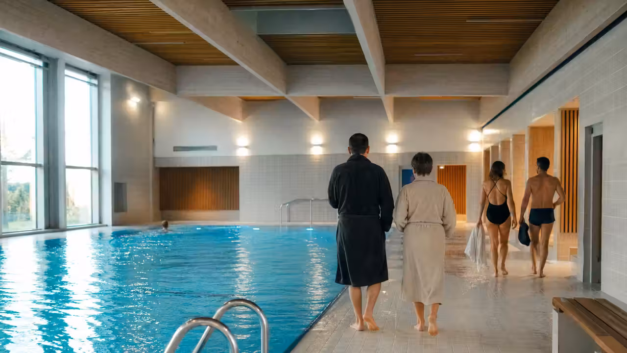 Bassin intérieur rénové d’une piscine municipale française, avec vestiaires modernes visibles au second plan