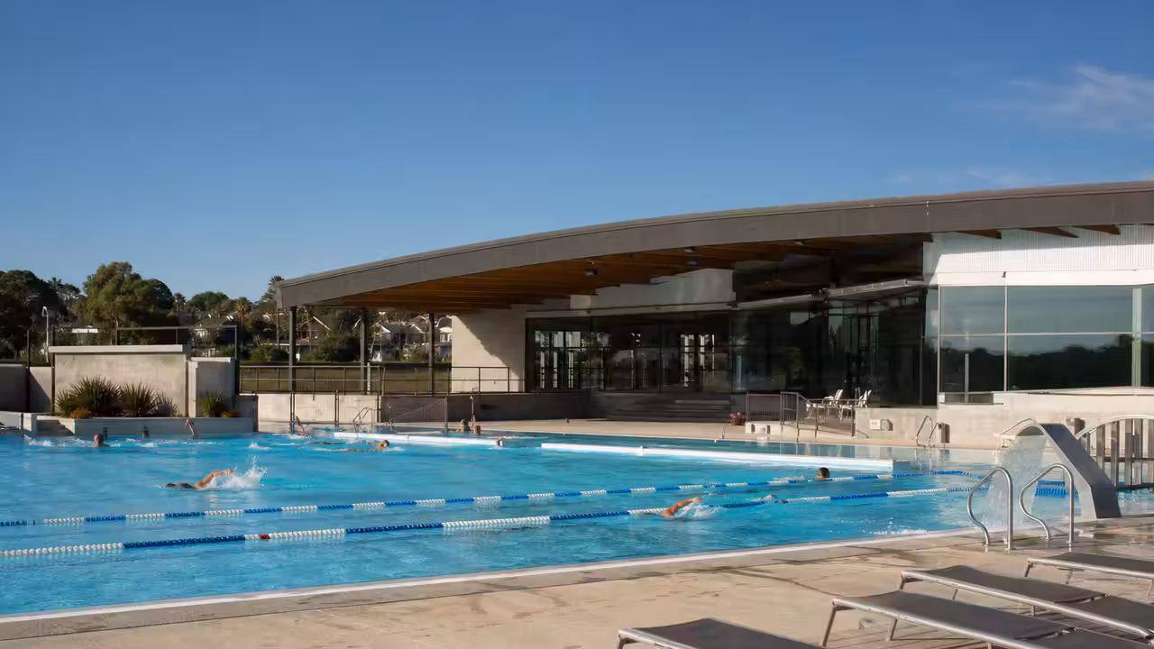 Bassin extérieur d’une piscine municipale avec bâtiment couvert, lignes d’eau et transats par une journée d’été