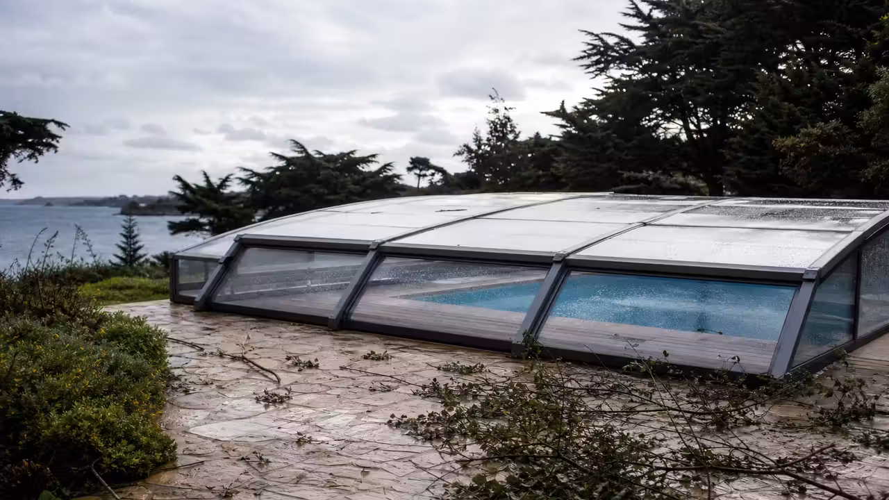 Abri de piscine fermé dans un jardin côtier après une tempête, avec quelques branches au sol