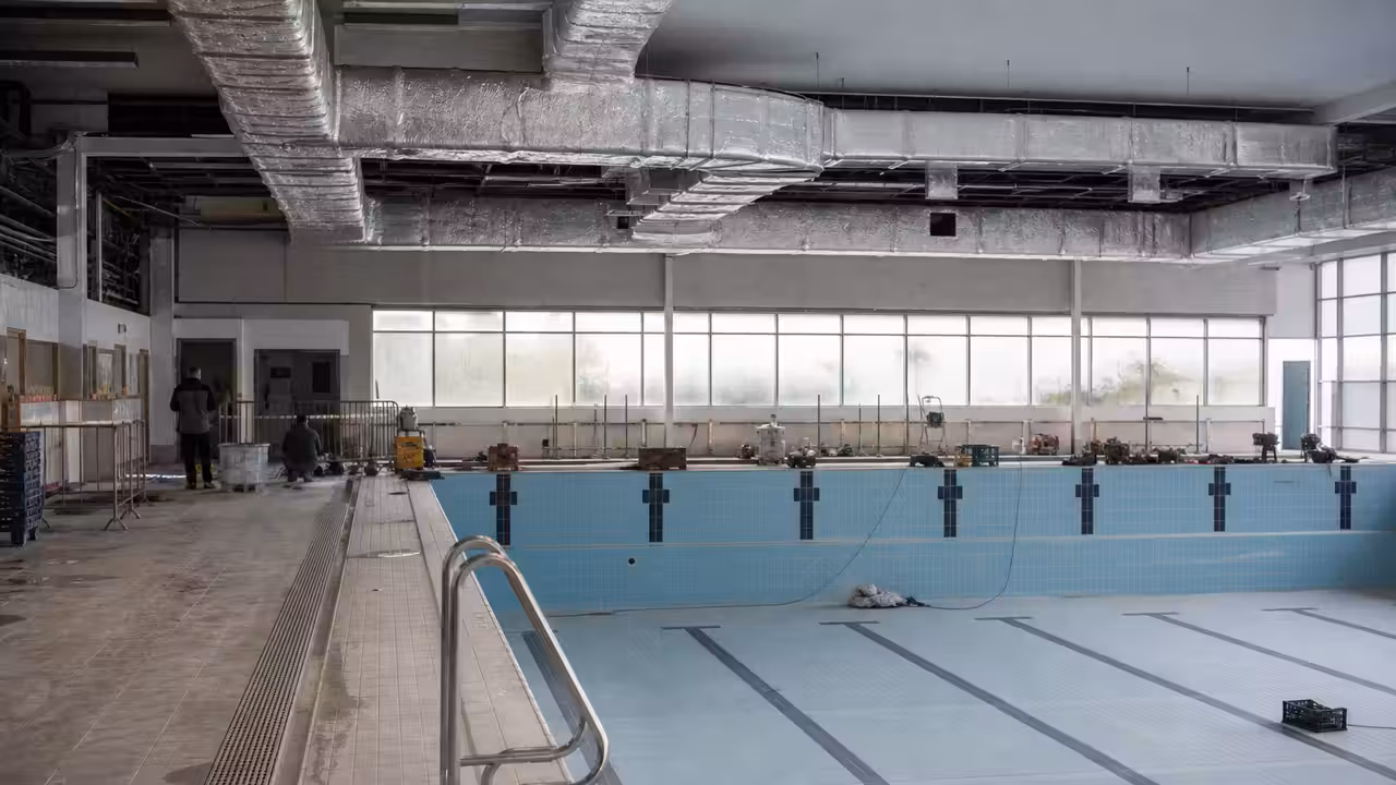 Bassin municipal couvert en rénovation, avec structure métallique, baies vitrées et équipements techniques visibles