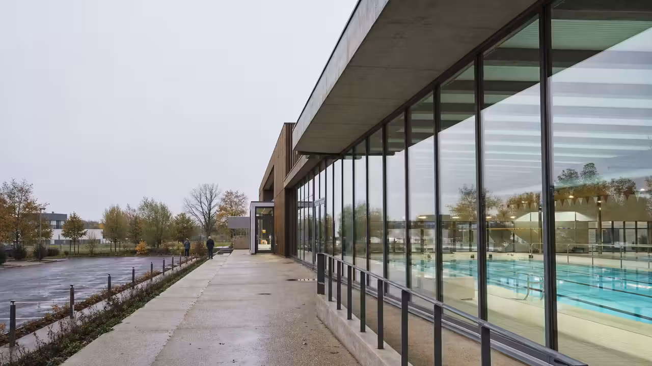 Vue extérieure d’un centre aquatique municipal contemporain avec bassin visible derrière de larges baies vitrées