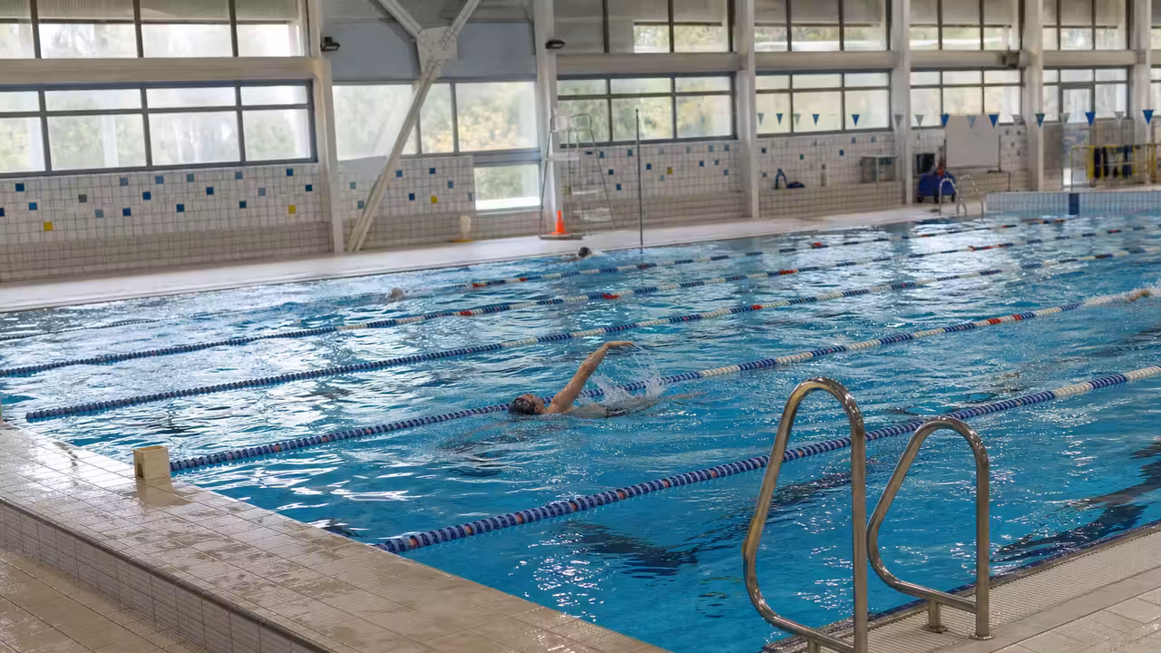 Nageurs dans un bassin couvert municipal aux lignes d’eau dégagées, vus depuis le bord de la piscine