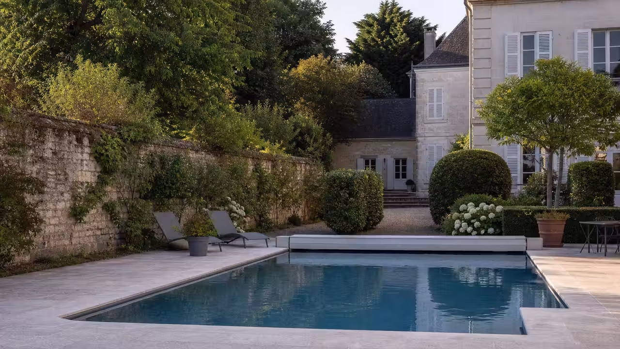 Piscine extérieure chauffée dans le jardin clos d’une demeure ancienne, avec terrasse minérale et végétation