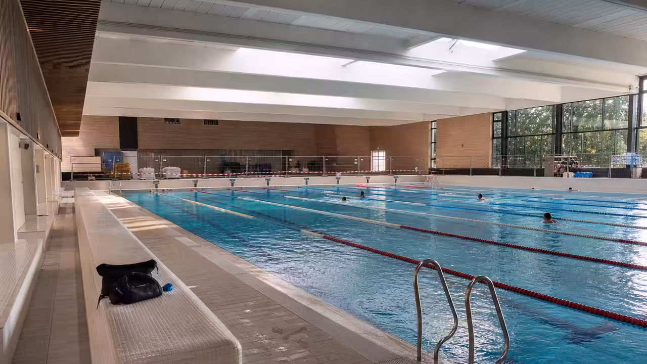 Lignes d’eau calmes dans une piscine municipale lumineuse, prêtes à accueillir un nombre limité de nageurs