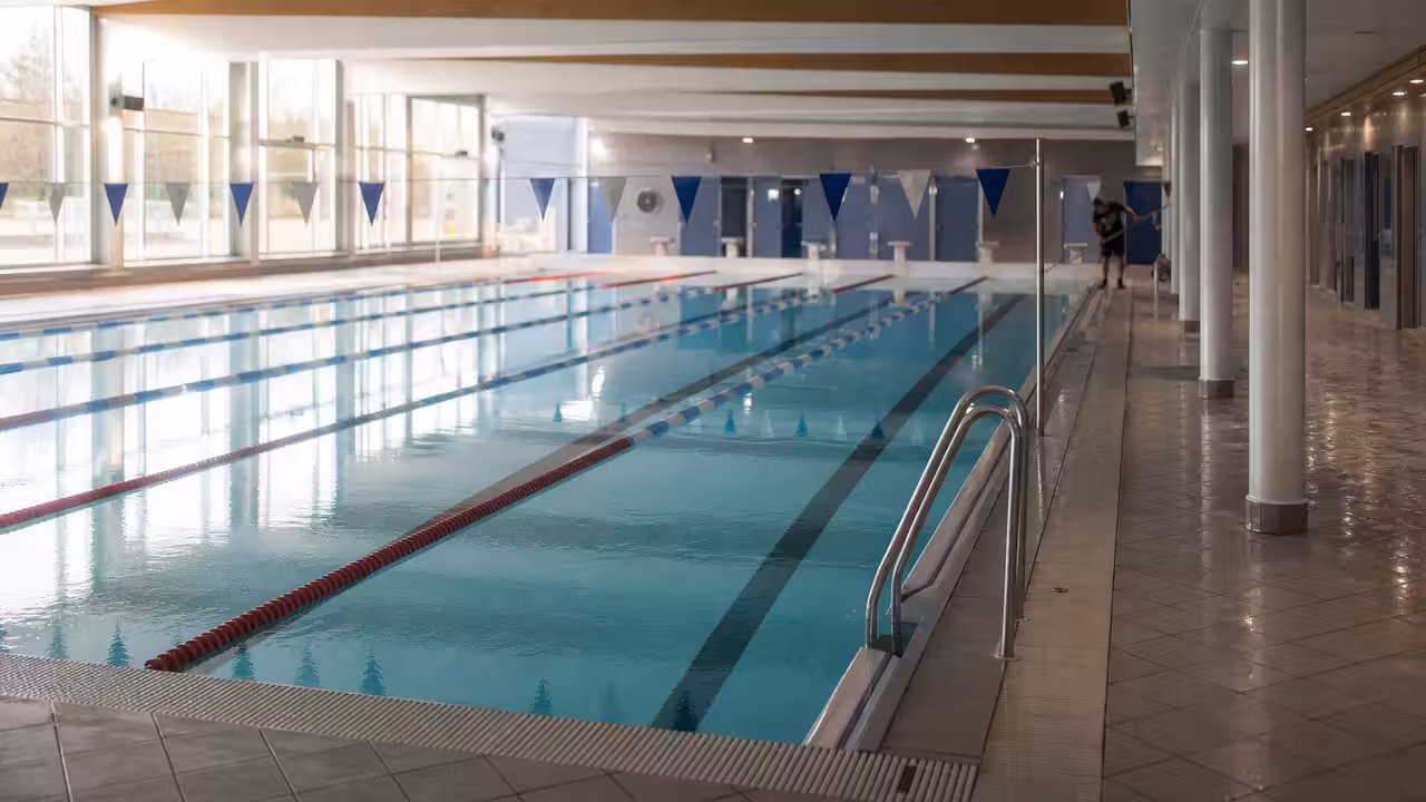 Bassin couvert d’une piscine municipale prêt à accueillir les nageurs, avec lignes d’eau et baies vitrées