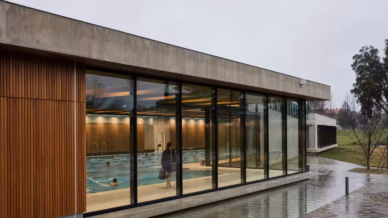 Façade contemporaine d’un centre aquatique municipal avec bassin intérieur visible et usagers de dos