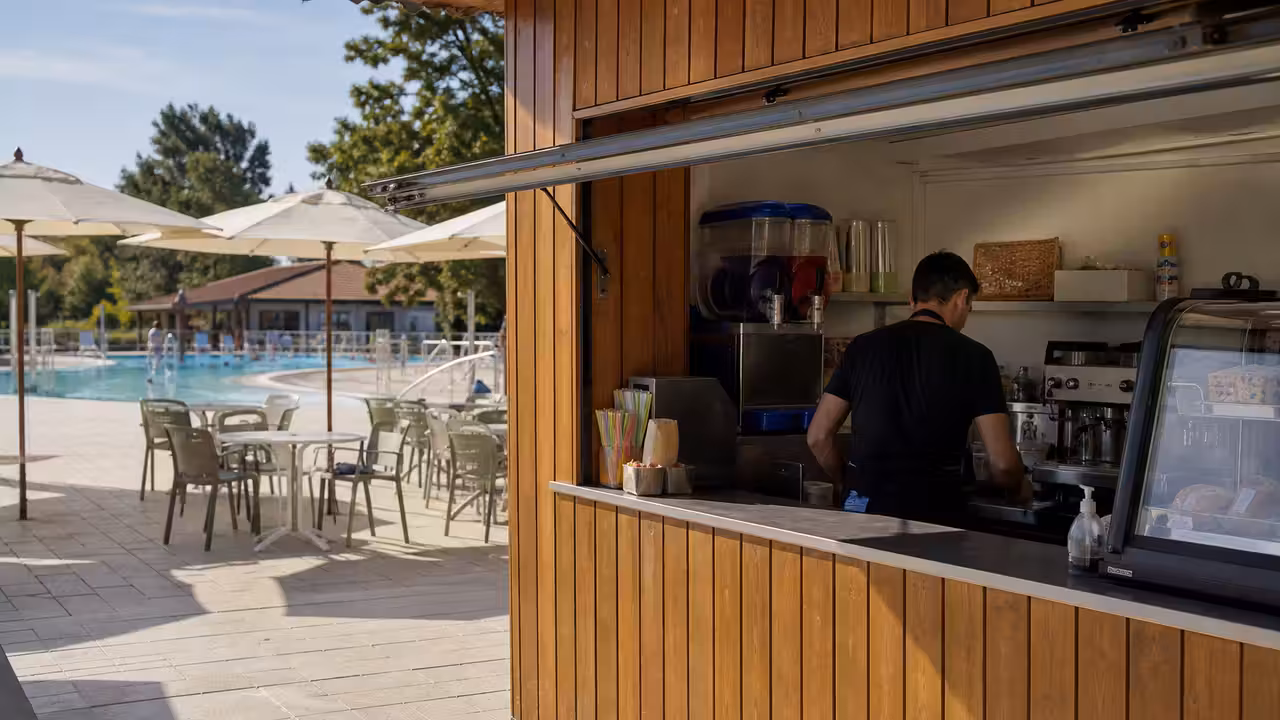 Comptoir de snack-bar saisonnier et tables ombragées à proximité d’une piscine municipale en été