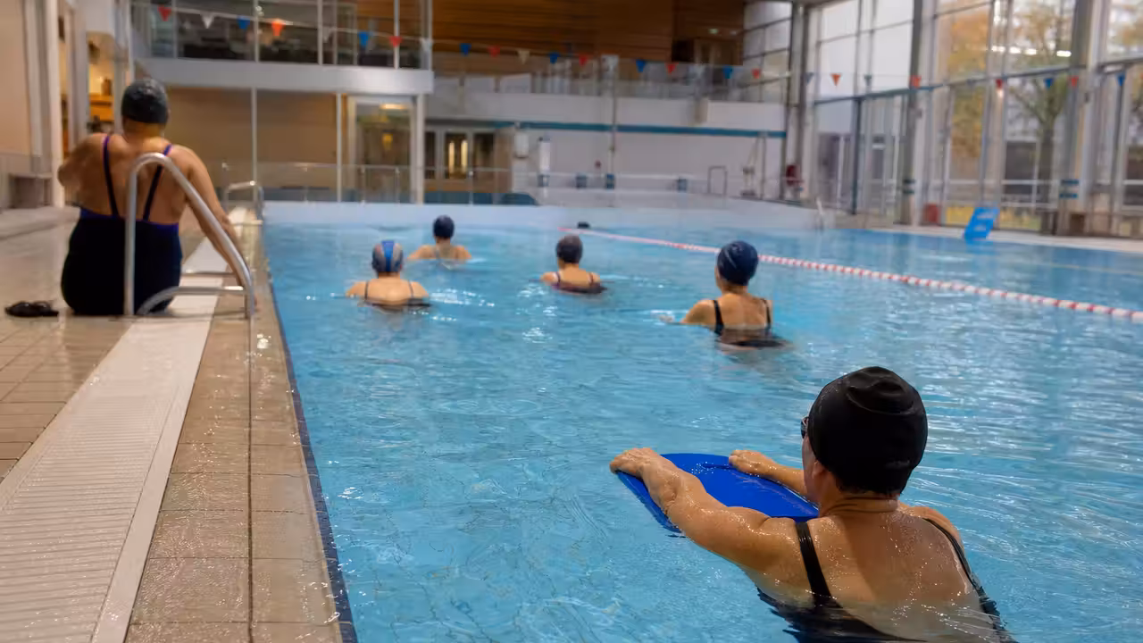 Bassin intérieur de piscine municipale avec lignes d'eau et nageurs encadrés pendant une séance d'apprentissage