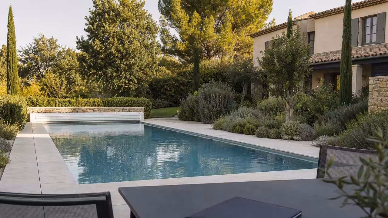 Propriétaire consultant les plans d’un bassin enterré devant une piscine dans un jardin résidentiel.
